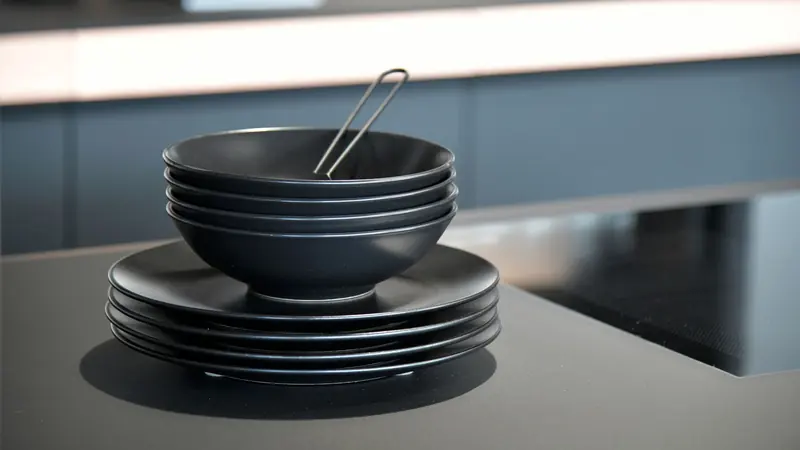 A stack of dark plates and bowls on a kitchen counter