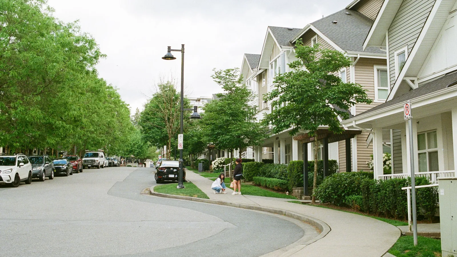 A curving residential street lined with trees, townhouses and parked cars