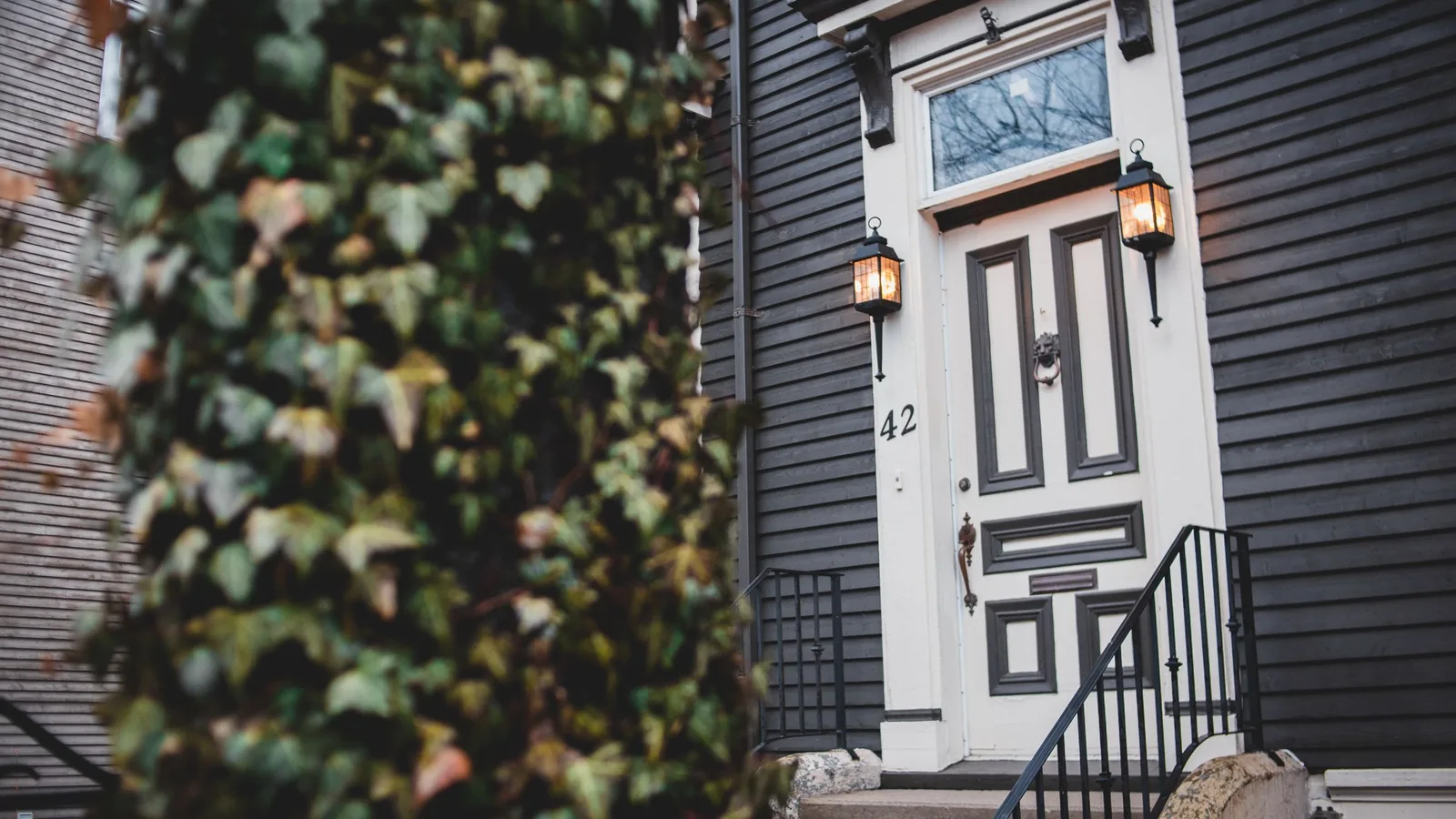 The front door of a house with lit lanterns, a short set of concrete steps and a black metal railing